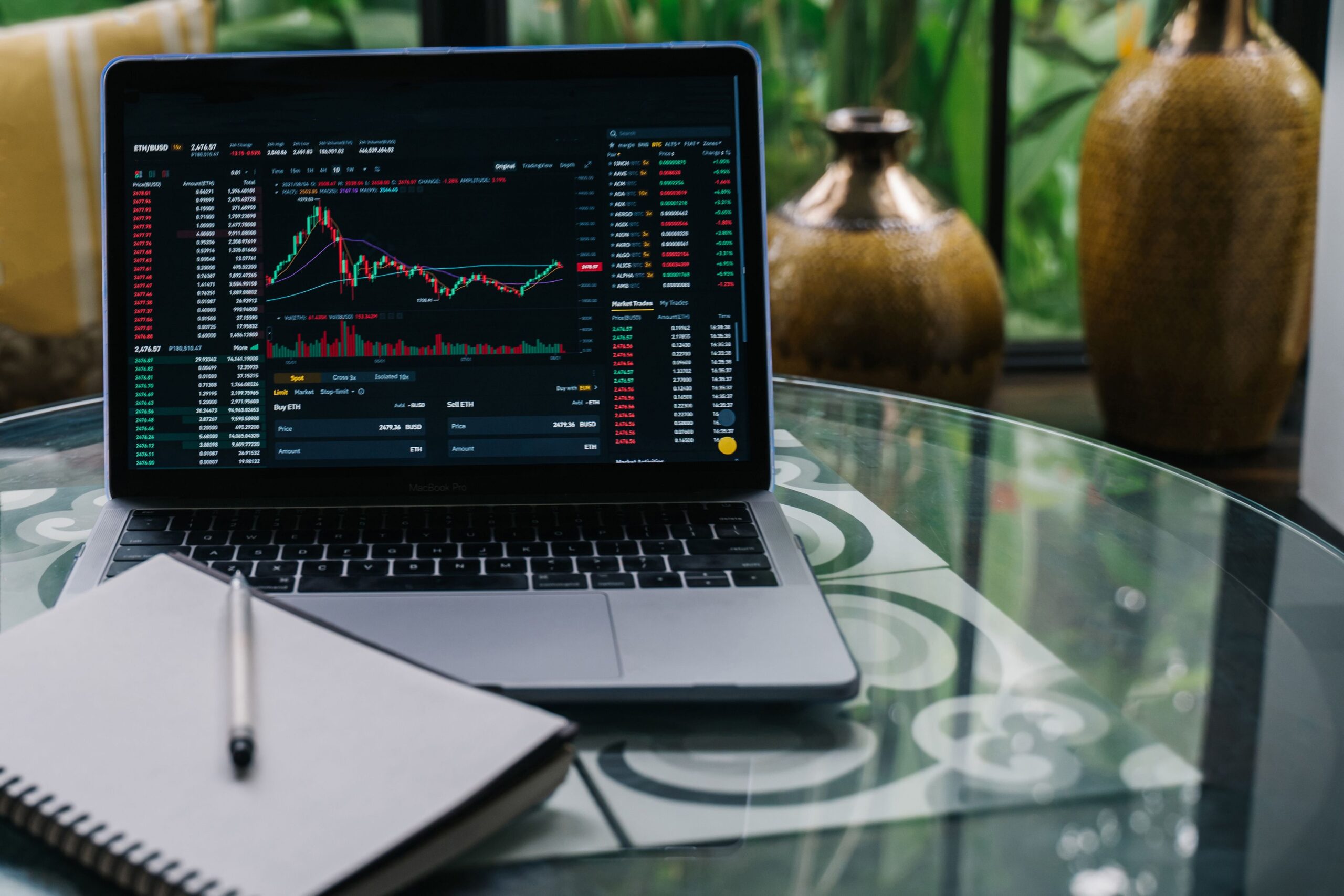 HOME Laptop displaying cryptocurrency stocks and graphs on a glass table with a notepad.