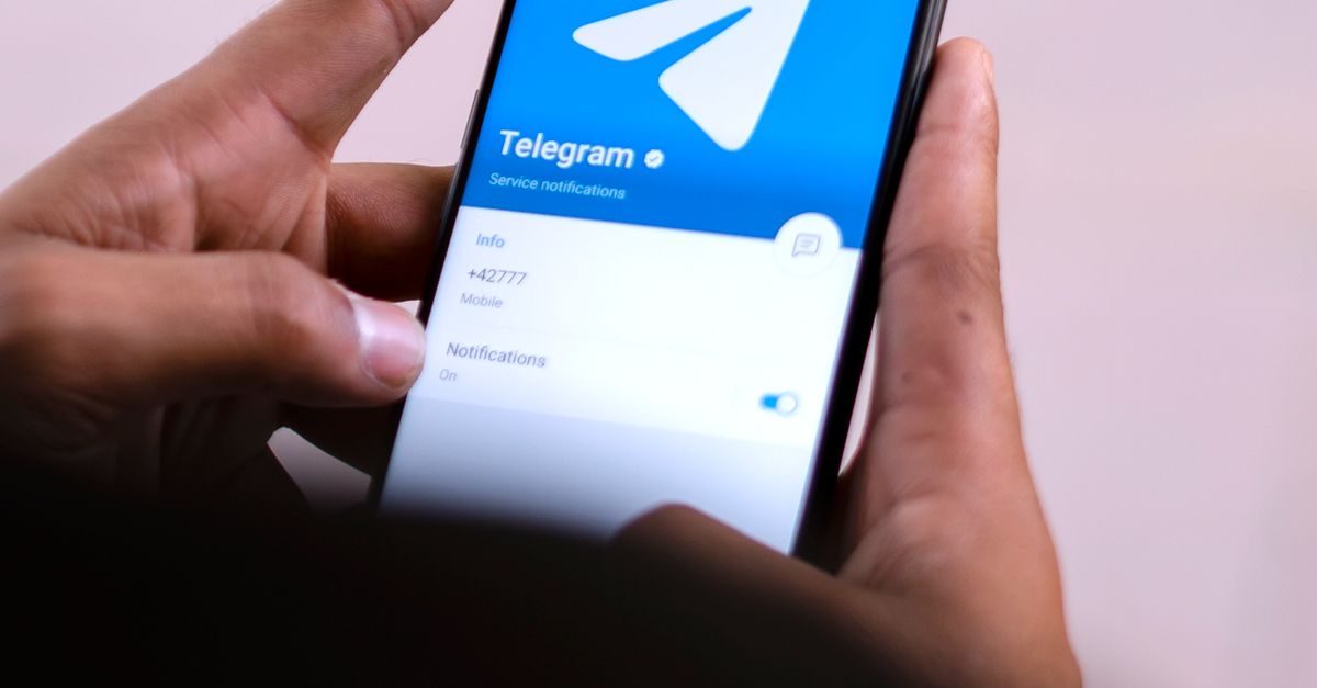 HOME Close-up of hands holding a smartphone with the Telegram app open on the screen.