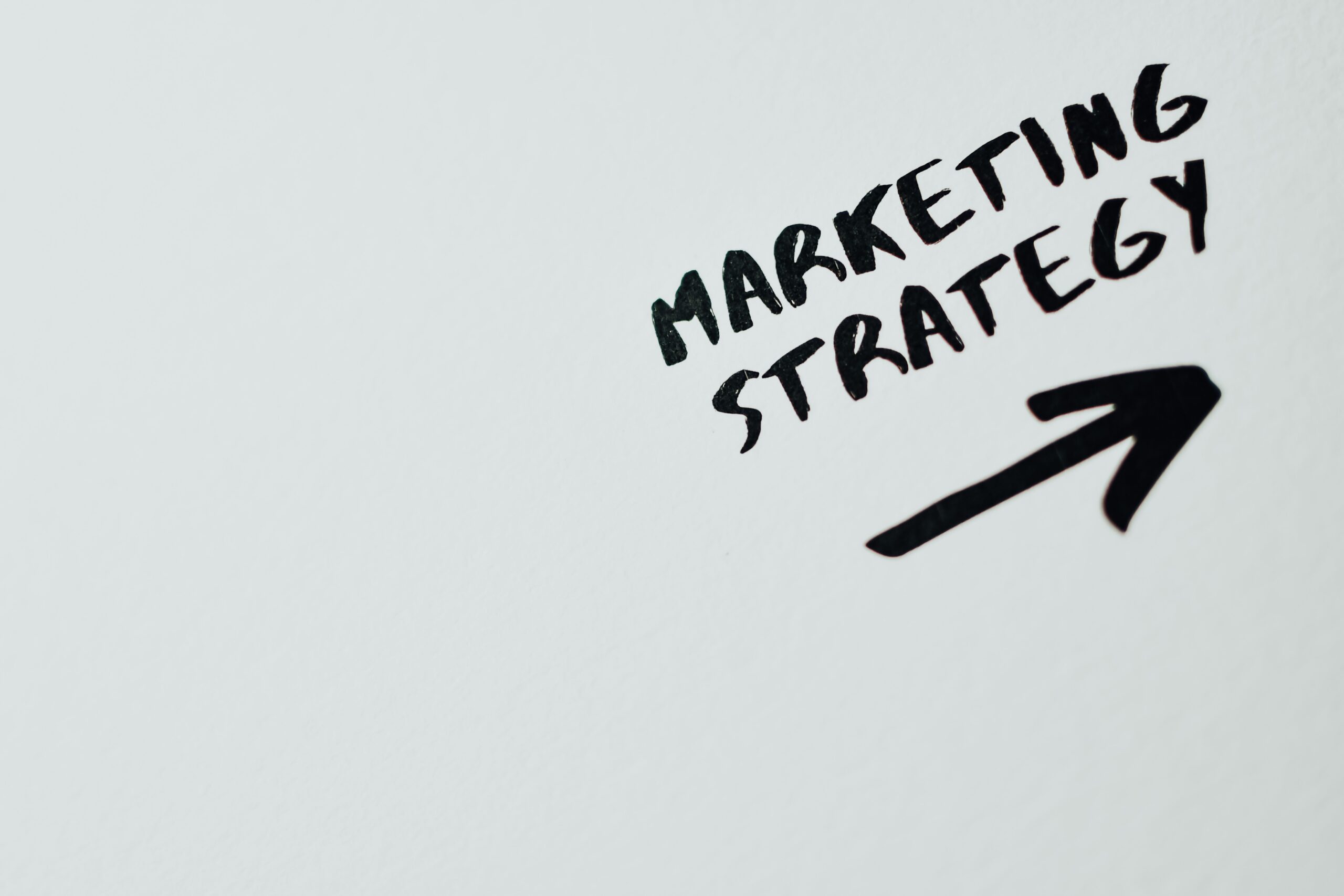 HOME Close-up of handwritten 'Marketing Strategy' text with an arrow on white background.